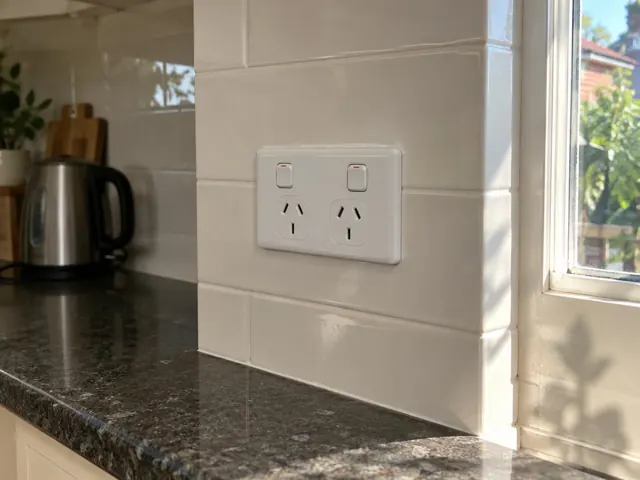 Double power point on tiled kitchen splashback beside a window and stone benchtop in Cammeray