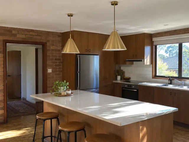 Kitchen with two brass pendant lights over a stone island, timber cabinets and brick walls in St Leonards
