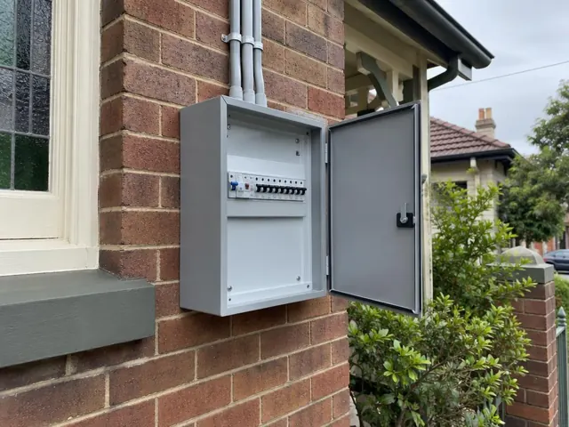 Outdoor switchboard cabinet on a brick exterior wall beside a window in Naremburn